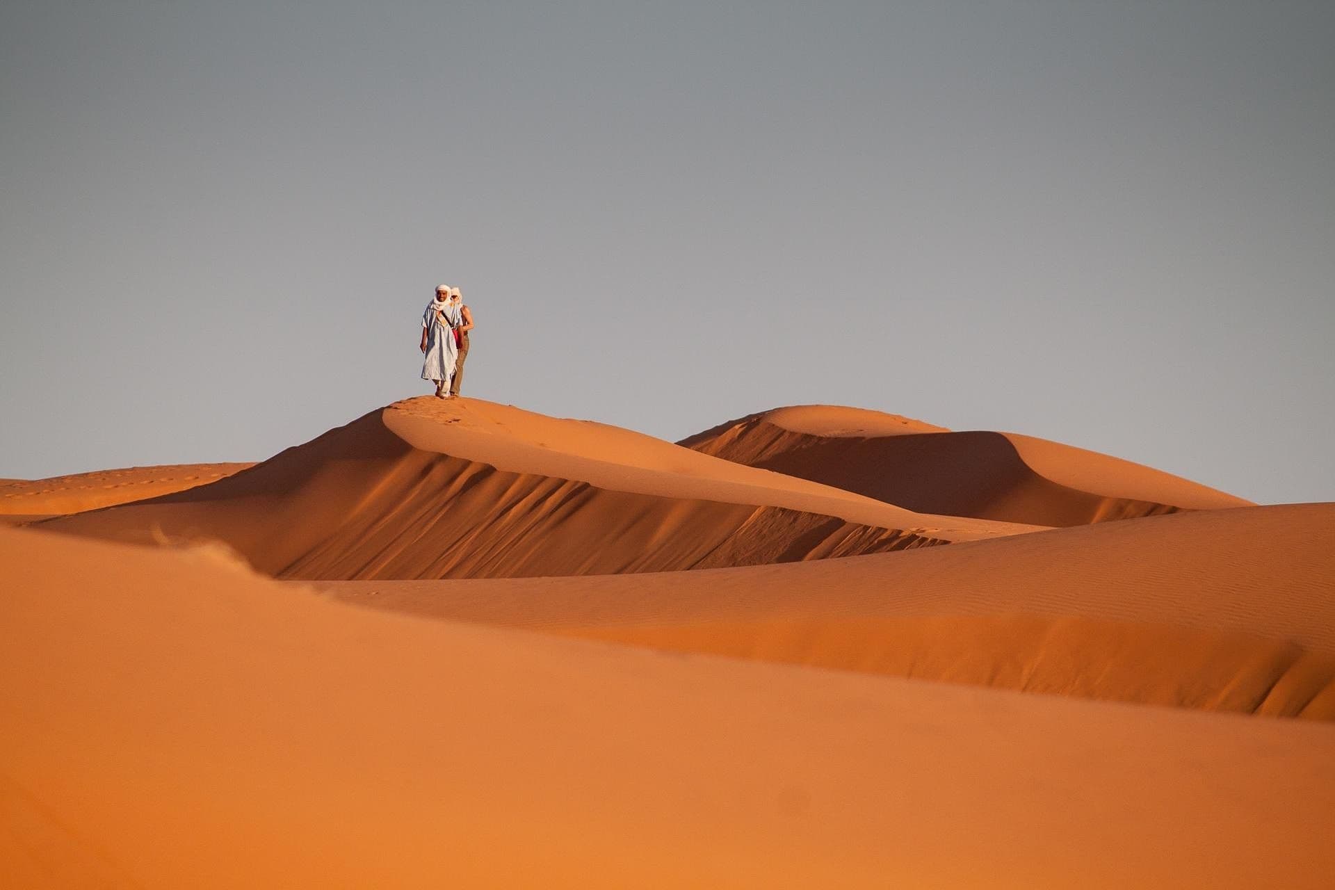 A lone figure standing on the crest of an orange dune