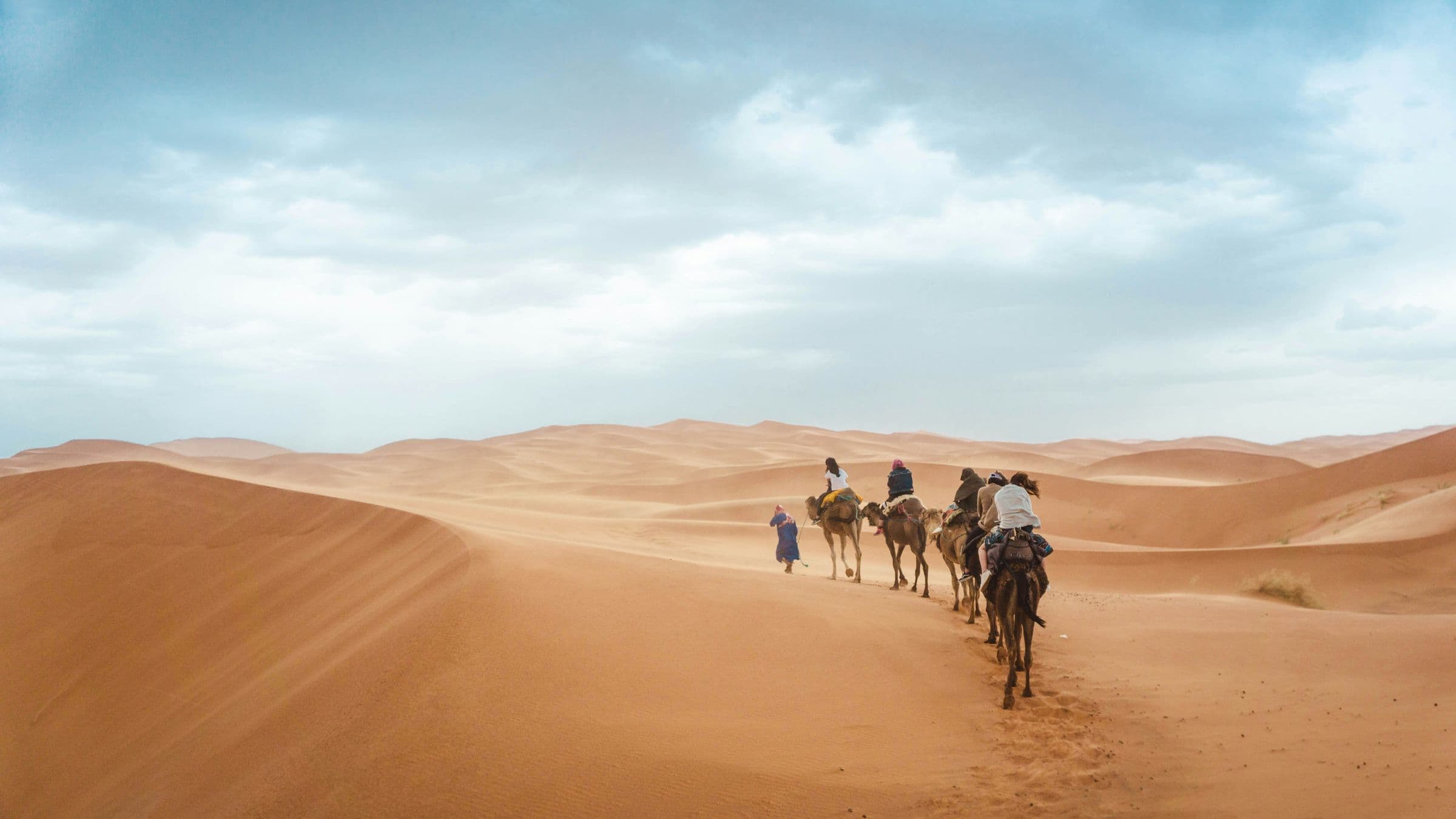 A line of travellers crossing high sand dunes under a pale sky