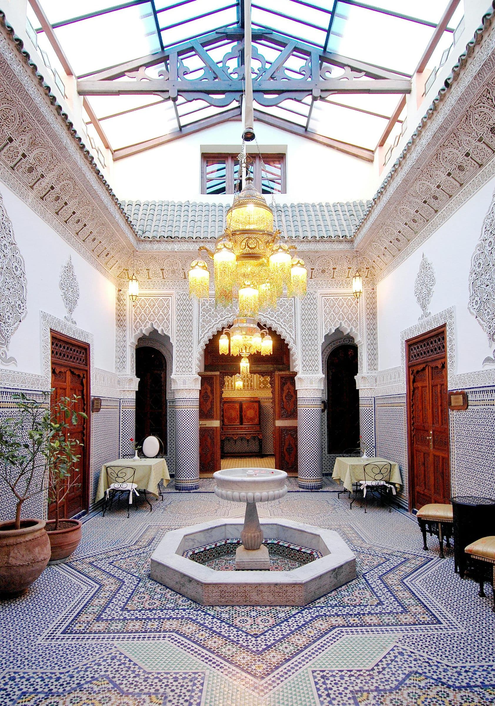 A carved plaster riad courtyard with a fountain, zellige tiles and cedar doors